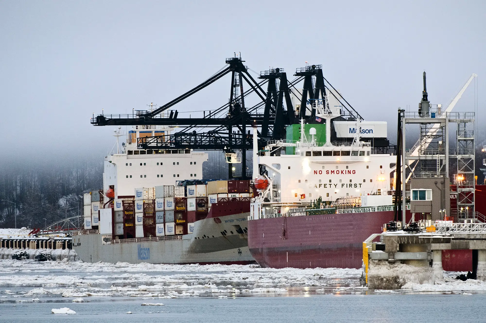 Container ships docked at an icy Alaskan port with cranes, illustrating how U.S. tariff policies impact American shipping and Alaska's unique freight logistics.